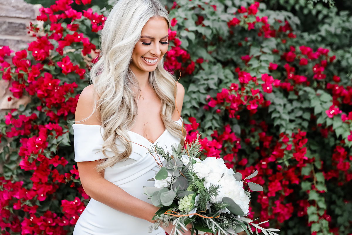 smiling bride in an off-shoulder wedding dress holding a white rose bouquet