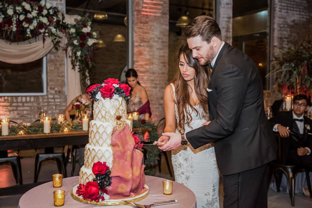 Handsome groom and pretty bride cutting a four tiered wedding cake decorated with roses